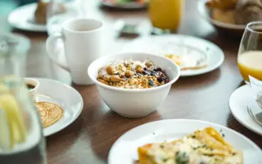 Auf einem gedeckten Frühstückstisch steh zwischen Eierspeisen und Pancakes eine Müslischale.