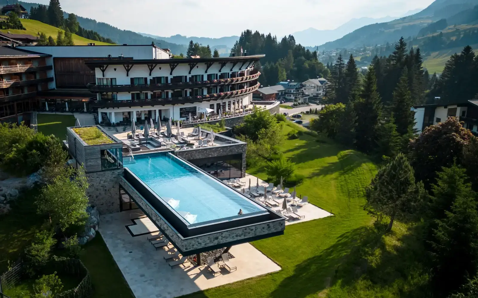 Ifen Kleinwalsertal Außenpool umgeben von einem großen Gebäude und Bäumen.