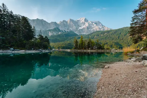 Eibsee Ein Gewässer mit Bäumen und Bergen im Hintergrund.