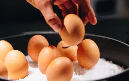Frühstückseier aja Eine Hand greift nach einem Ei in einer Schale mit Salz.