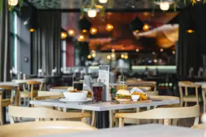 Ein Restaurant mit Tischen und Stühlen. Im Fokus steht ein Tisch mit Burger und Softdrinks angerichtet.