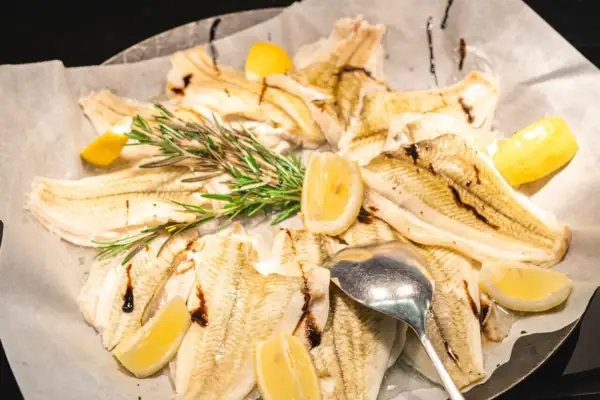 Fisch Ein Teller mit Fisch und Zitronenscheiben, daneben ein Löffel.