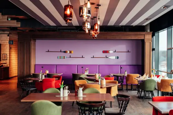 Restaurant im aja Grömitz Ein Raum mit Tischen und Stühlen und einer lila Wand mit Rudern.