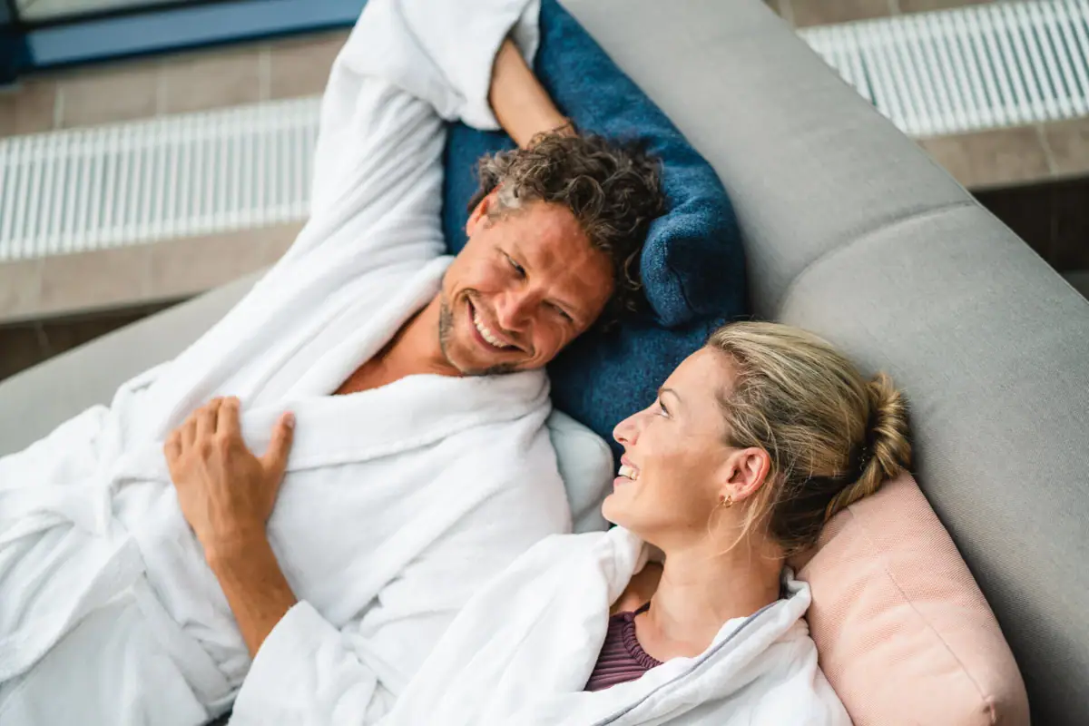 Ein Mann und eine Frau liegen lächelnd auf einem Sofa.