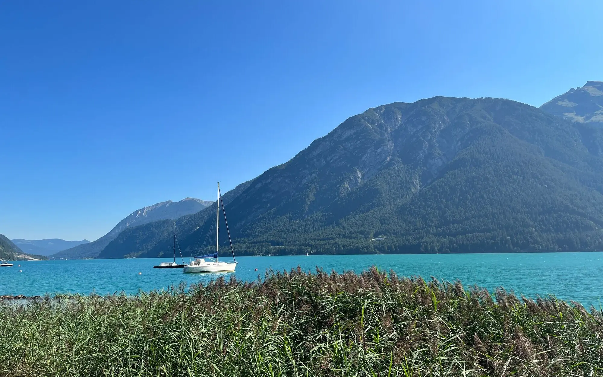 Segelboot auf einem See mit Bergen im Hintergrund.