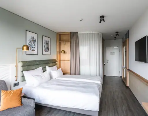 Neue Zimmer im aja Warnemünde Hotelzimmer mit Doppelbett, Kissen und Bettwäsche.