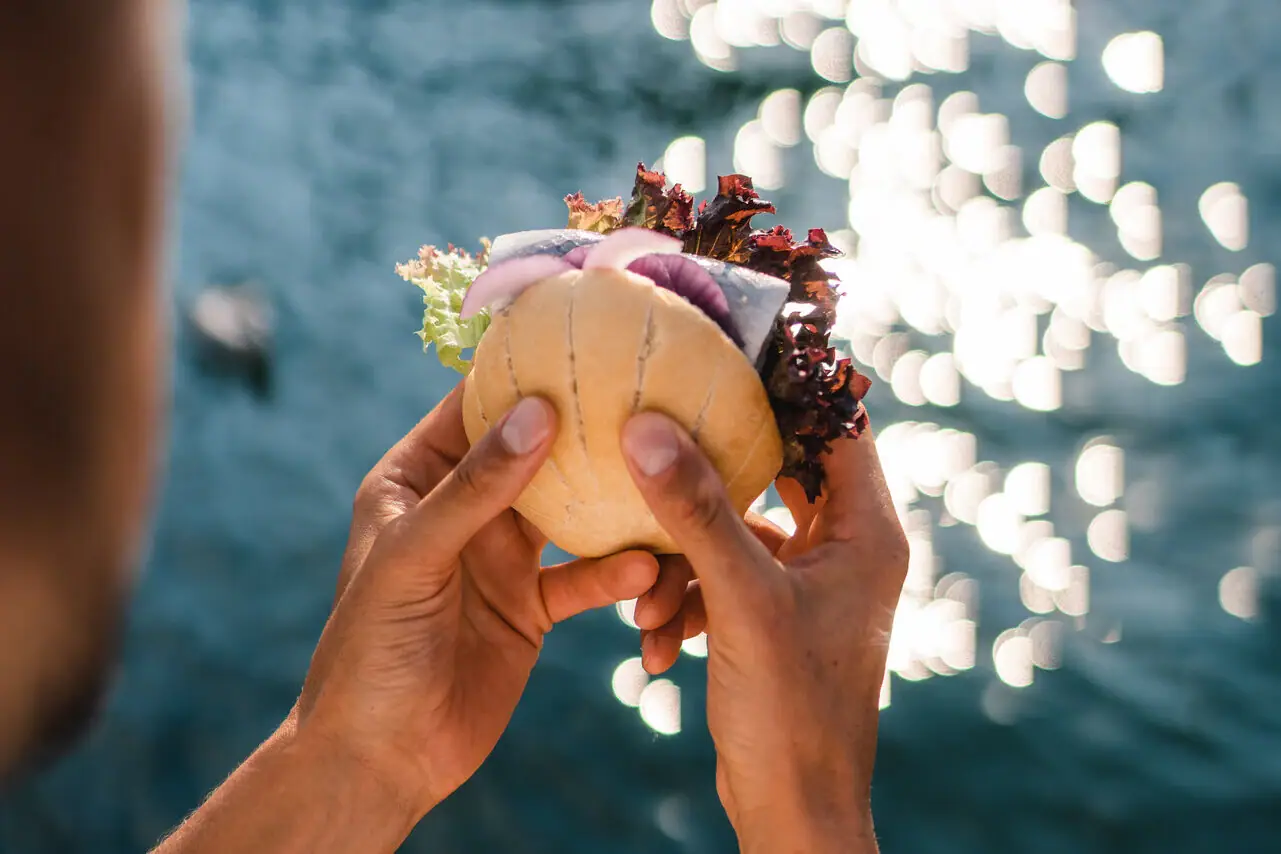 Eine Person hält ein Fischbrötchen über Wasser.