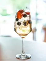 Ein hohes Glas, gefüllt mit einem hellen Sprudelgetränk, Blaubeeren und Erdbeeren steht auf einem grauen Untergrund.