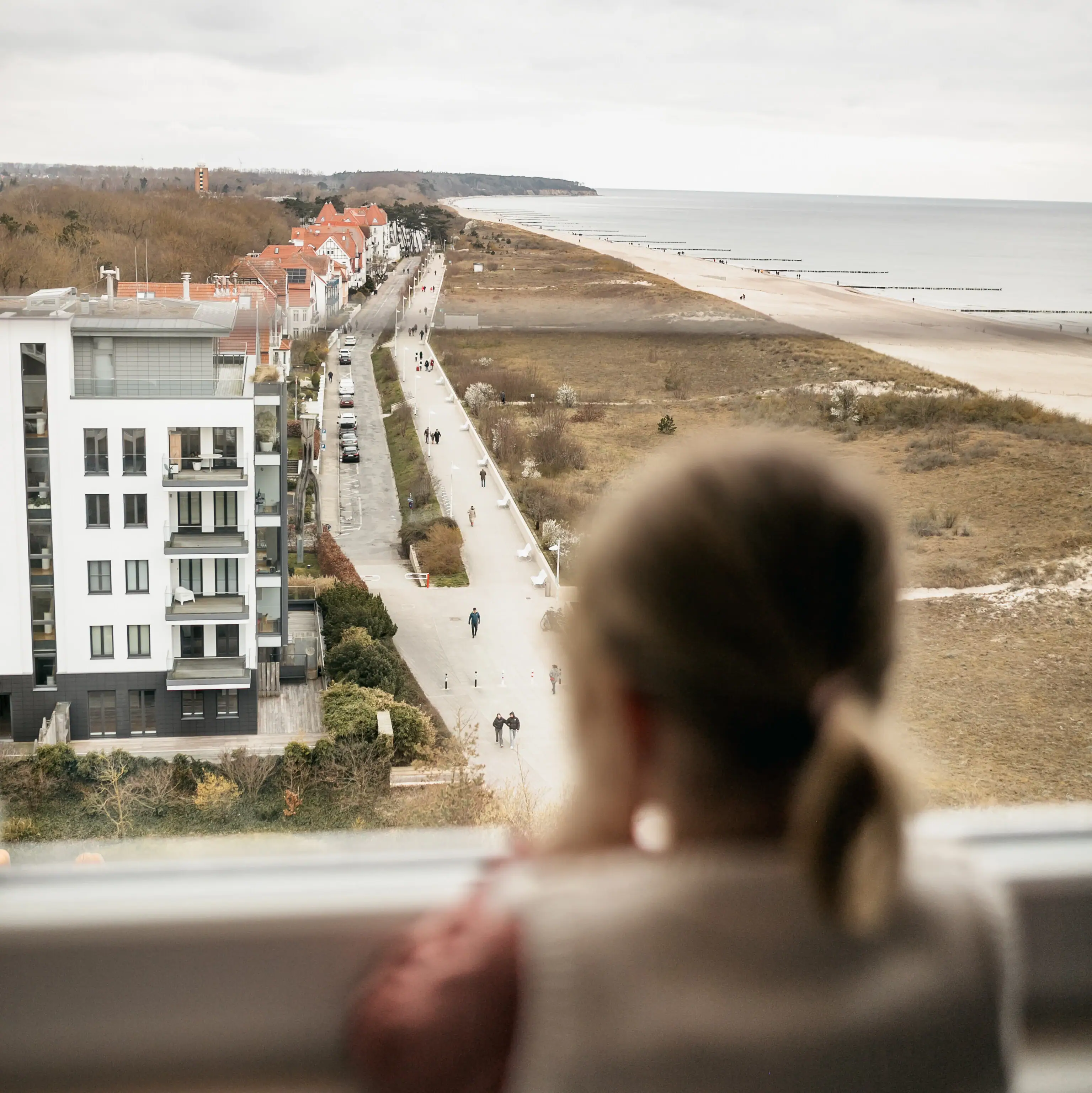 Zimmerausblick Ein Mädchen blickt aus einem Fenster auf einen Strand.