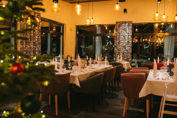 Silvesterabend im aja Ruhpolding Ein Raum mit Tischen und Stühlen, festlich dekoriert und im Vordergrund in der Unschärfe steht ein Weihnachtsbaum.