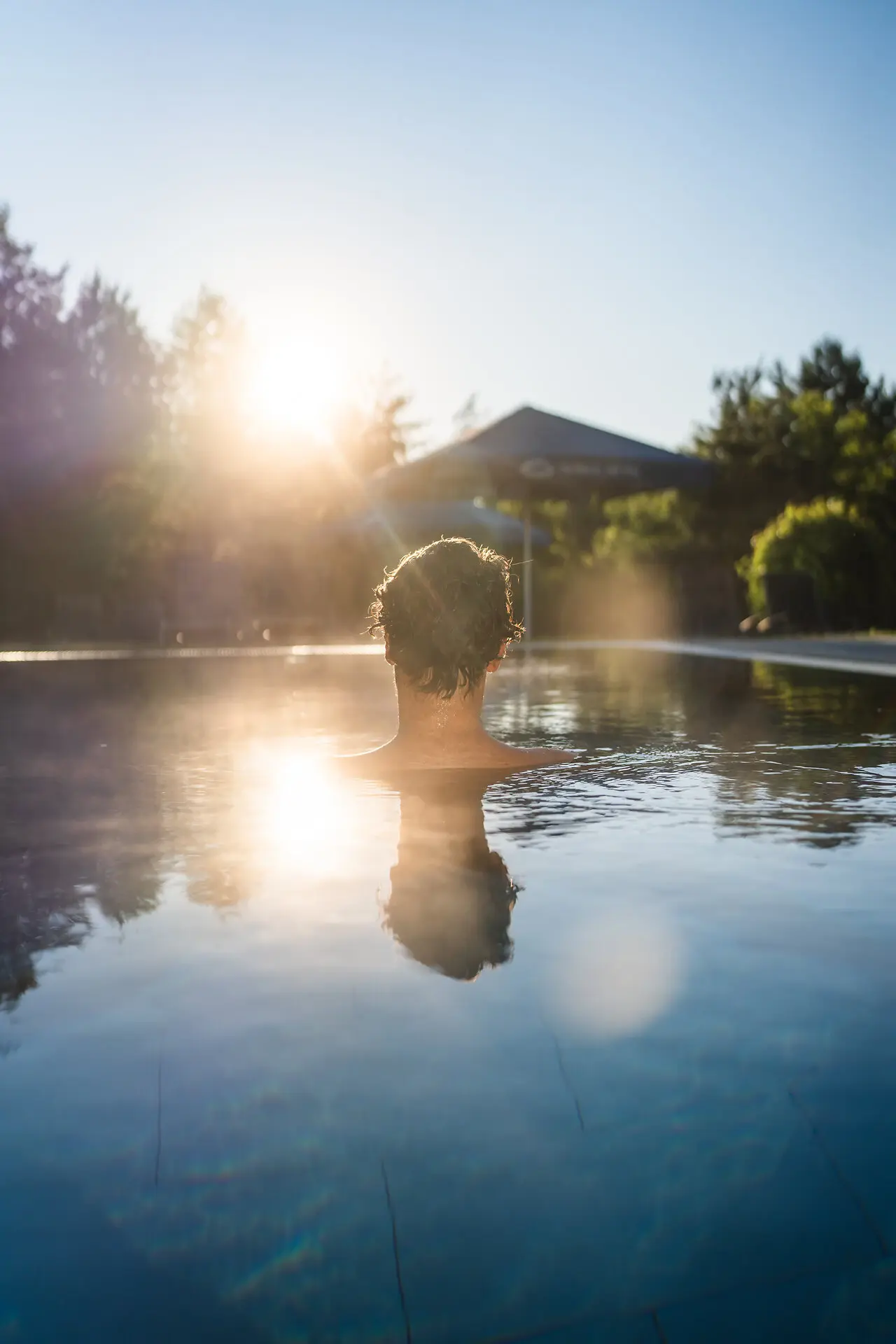 Außenpool in Bad Saarow Person im Pool, umgeben von Natur mit Sonnenlicht.