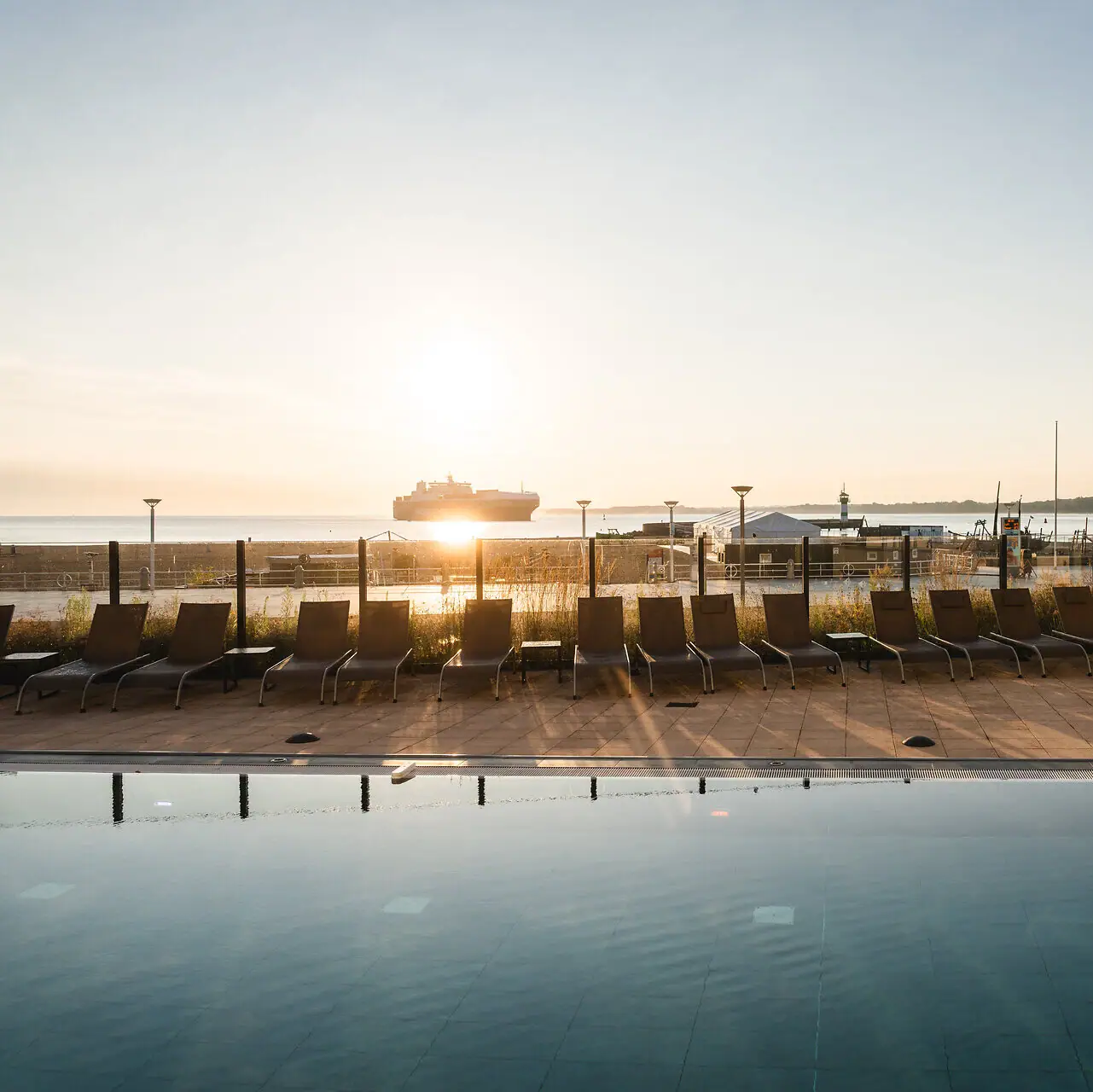 Außenpool aja Travemünde Ein Pool mit Stühlen und einem Boot im Hintergrund.