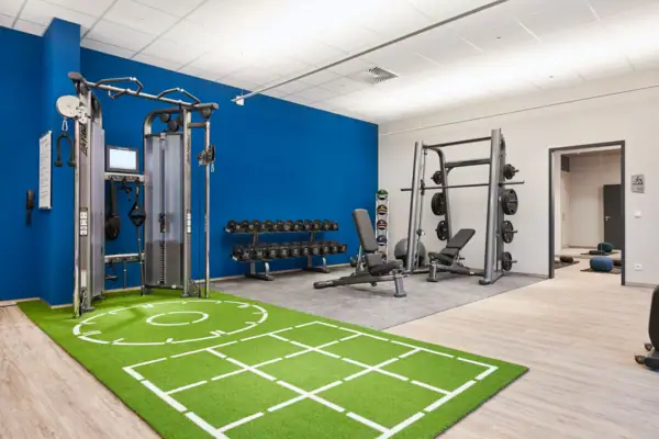 Fitnessraum Fitnessstudio mit Trainingsgeräten und grünem Teppichboden