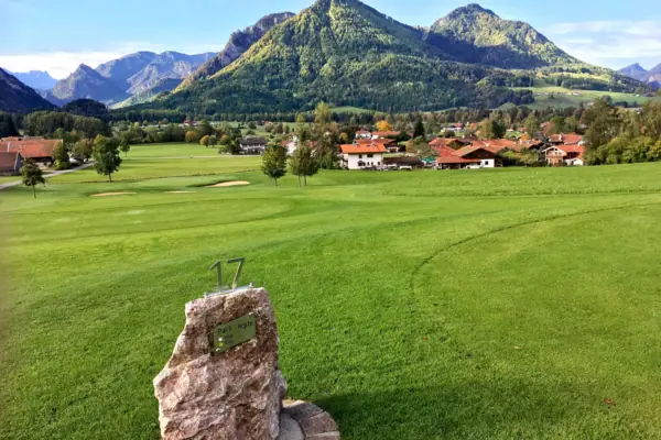 Golfplatz Ruhpolding Ein Stein auf einer Wiese mit einer Gruppe von Häusern im Hintergrund.