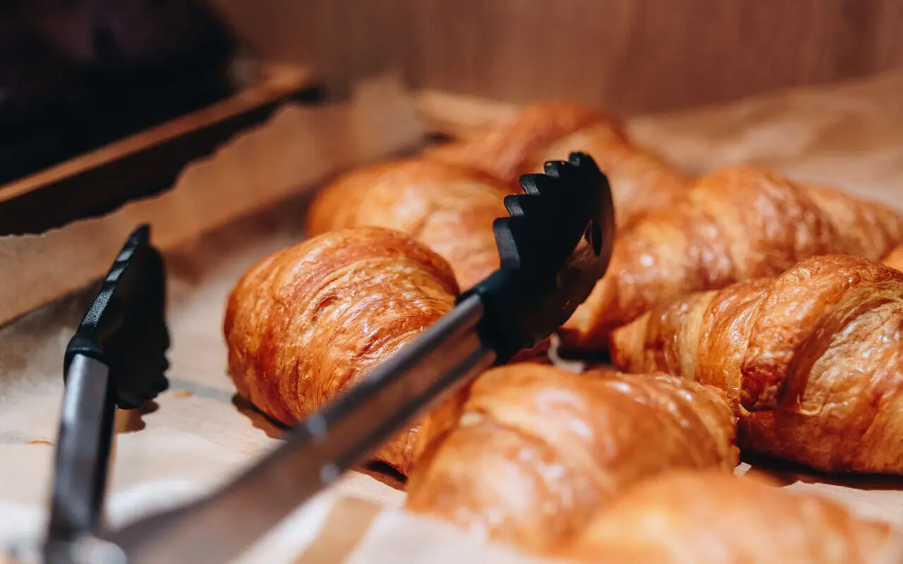Croissants Auf einem Backblech liegen braun gebackene Croissants und eine Auffüllzange.