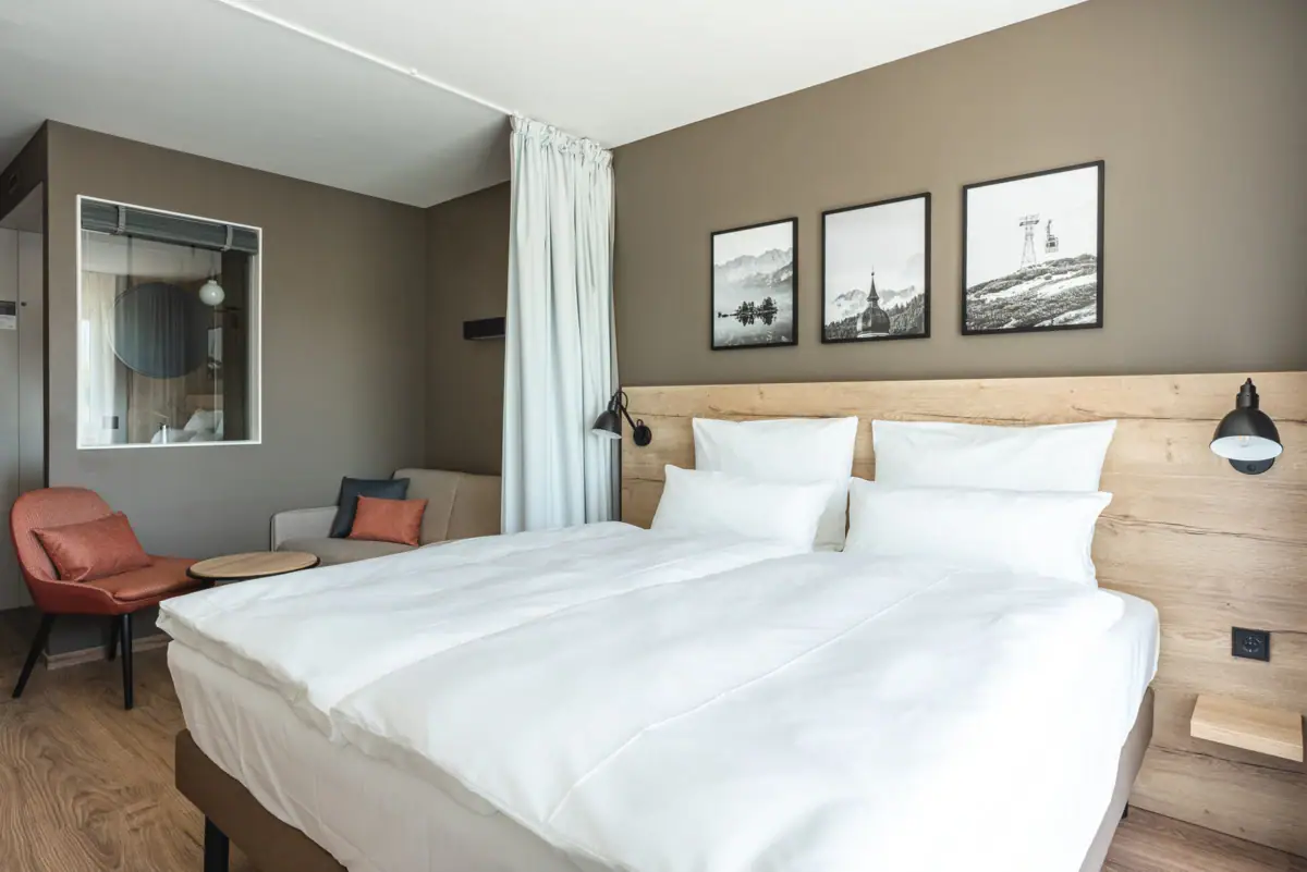 Zimmer 118 Ein Bett mit weißen Bettlaken und ein Stuhl im Raum.