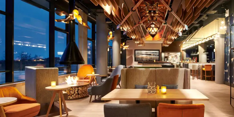 Ein stilvolles Restaurant mit moderner Einrichtung, gemütlichen Sitzgelegenheiten und einem warmen Ambiente. Ein offener Kamin sorgt für eine einladende Atmosphäre, während ein dekoratives hölzernes Ruderboot die Decke ziert. Ein stilvolles Restaurant mit moderner Einrichtung, gemütlichen Sitzgelegenheiten und einem warmen Ambiente. Ein offener Kamin sorgt für eine einladende Atmosphäre, während ein dekoratives hölzernes Ruderboot die Decke ziert.