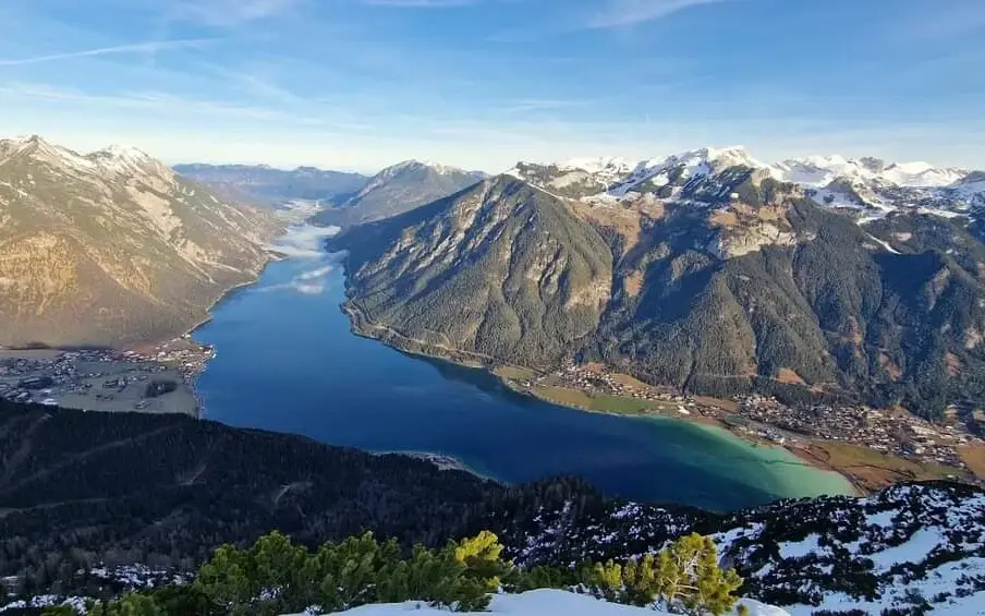 Der Achensee in einem Tal umgeben von Bergen und einer vielfältigen Landschaft.