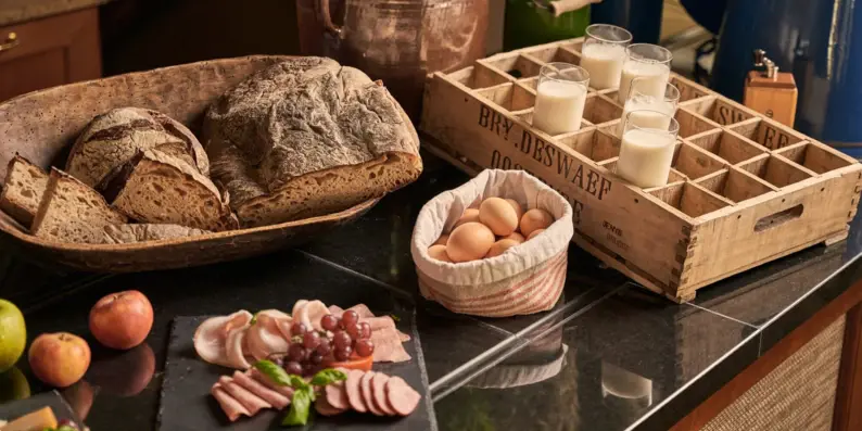 Ein Frühstücksbuffet mit einem großen Brotkorb, einer Wusrplatte, Frühstückseiern, Äpfeln und Gläsern mit Milch. Ein Frühstücksbuffet mit einem großen Brotkorb, einer Wusrplatte, Frühstückseiern, Äpfeln und Gläsern mit Milch.