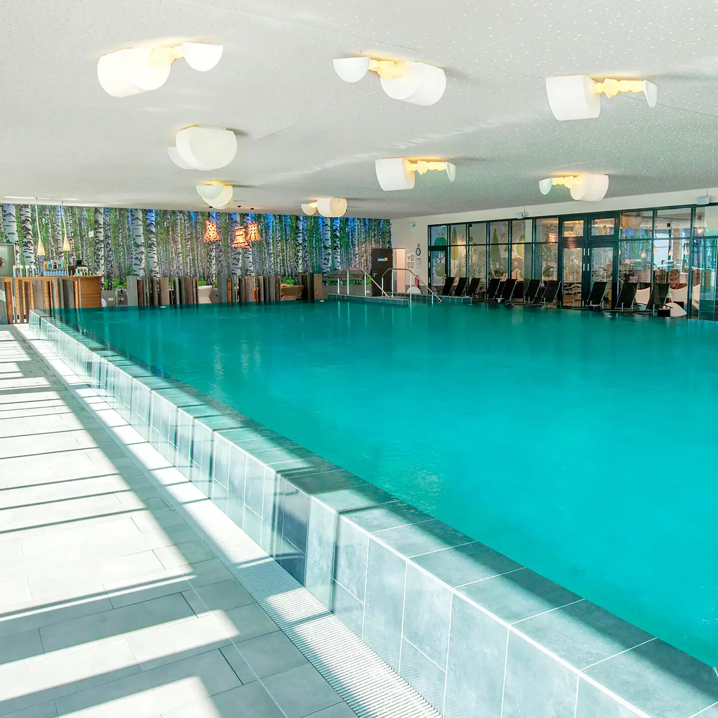 Pool im aja Bad Saarow Ein Schwimmbecken mit Stühlen und Tischen.