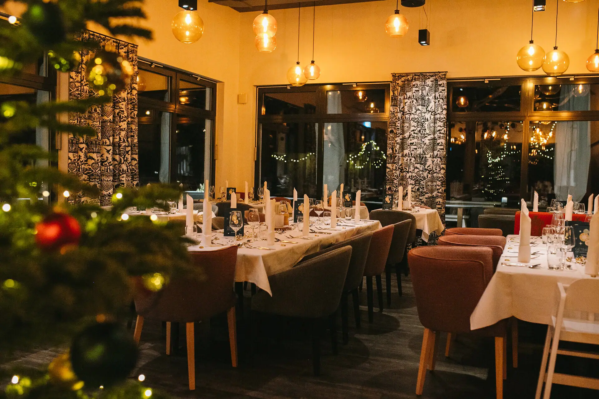 Silvesterabend im aja Ruhpolding Ein Raum mit Tischen und Stühlen, festlich dekoriert und im Vordergrund in der Unschärfe steht ein Weihnachtsbaum.