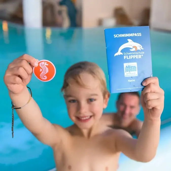 Schwimmschule Usedom Ein Junge hält ein Buch und eine Münze im Pool.