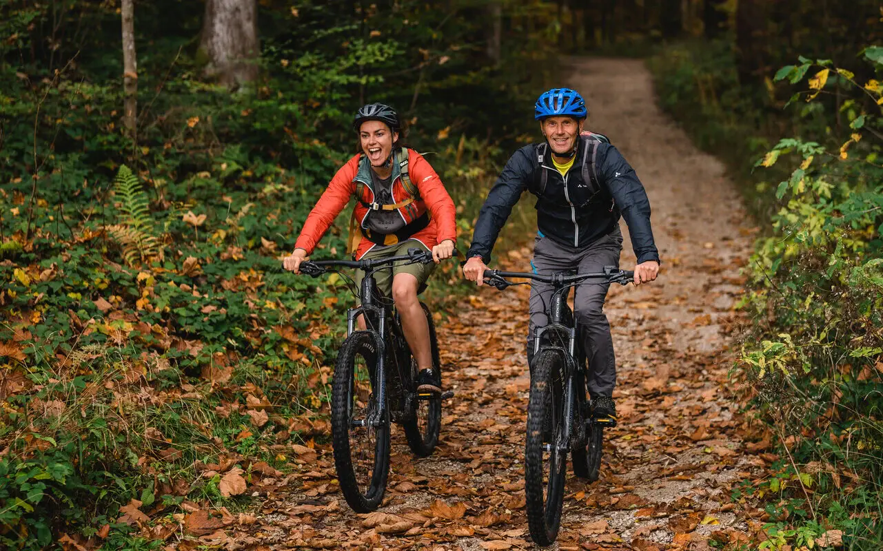 E-Bikes Ruhpolding Zwei Personen auf Mountainbikes fahren einen herbstlichen Weg entlang.