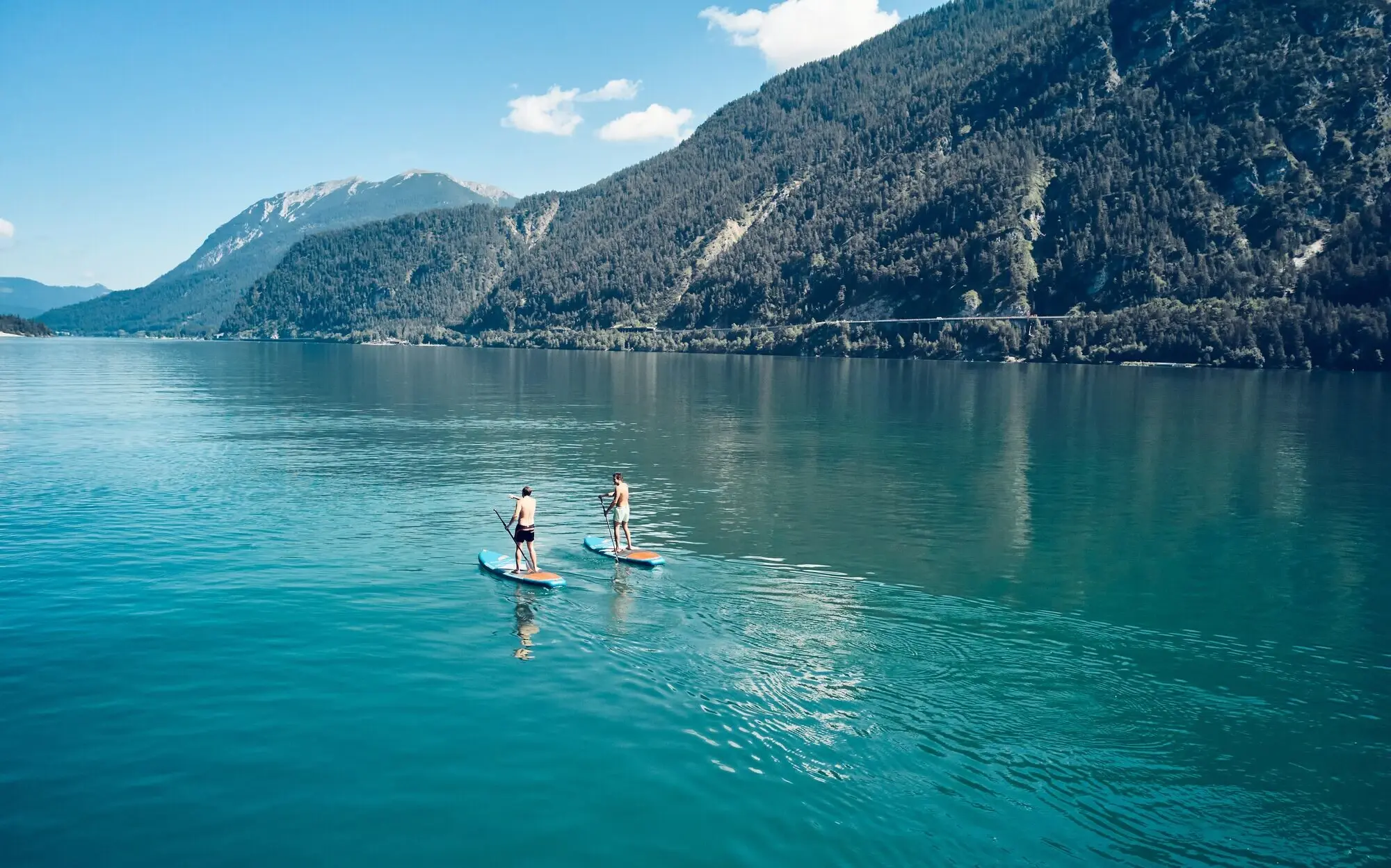 Zwei Personen auf Stand-Up-Paddleboards auf einem See.