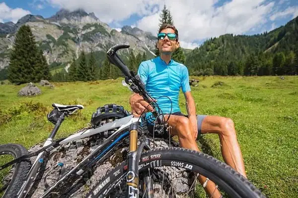 Mann sitzt auf einem Felsen mit seinem Fahrrad vor einer Bergkulisse.