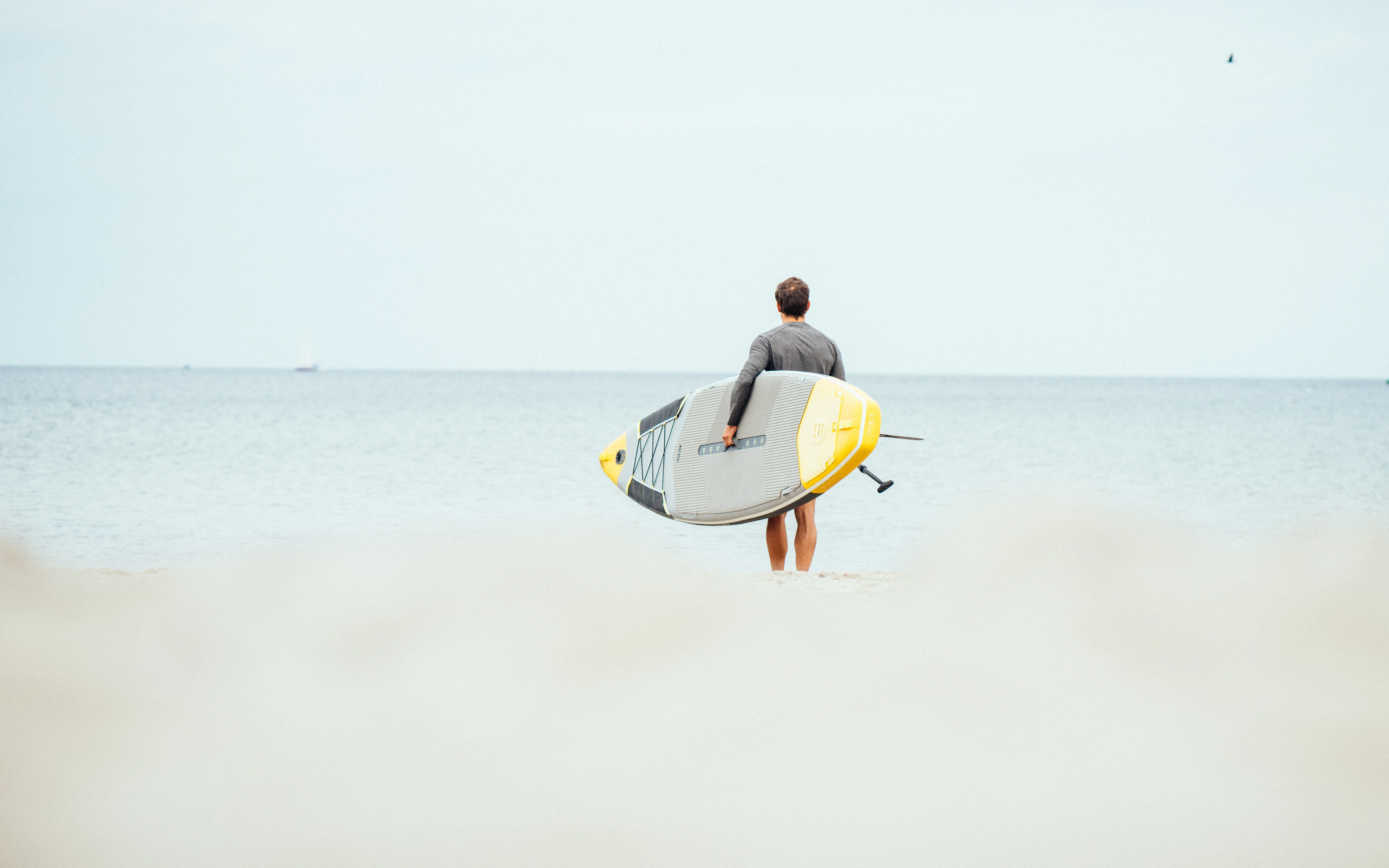 Ein mann geht knöcheltief ins Wasser und hat ein Surfbord unter den Arm geklemmt.