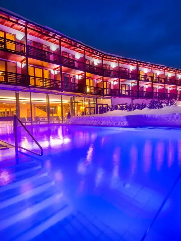 Außenpool bei Nacht Ein Gebäude mit einem Pool und Schnee im Vordergrund.