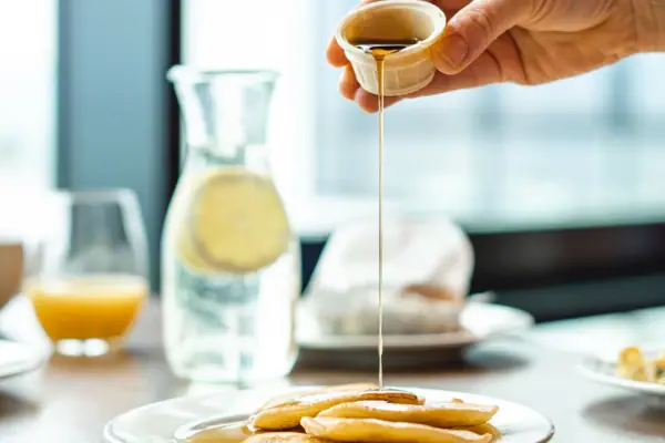 Frühstück Eine Person gießt Sirup auf einen Teller mit Pfannkuchen.