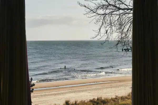 Ein Fenster mit Vorhängen, das auf einen Strand mit Sand blickt.