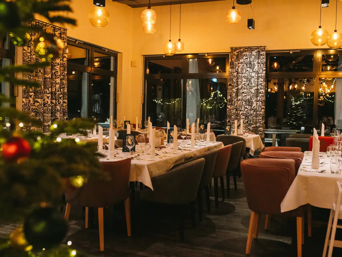 Silvester im aja Ruhpolding Ein Raum mit Tischen und Stühlen und einem Weihnachtsbaum.