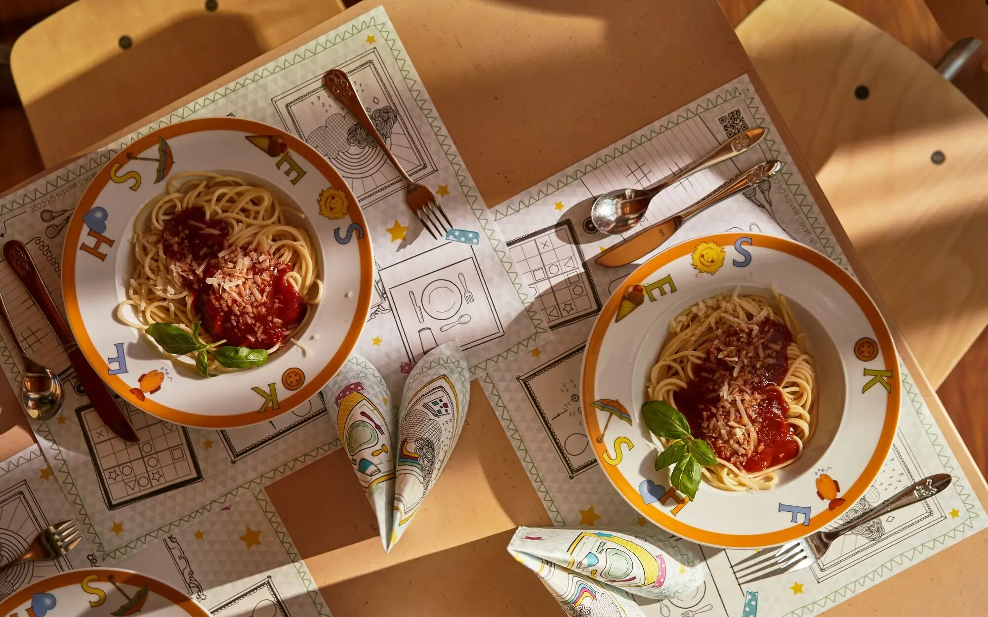 Kinder aja Bansin Teller mit Spaghetti, Sauce und Käse auf einem Tisch.
