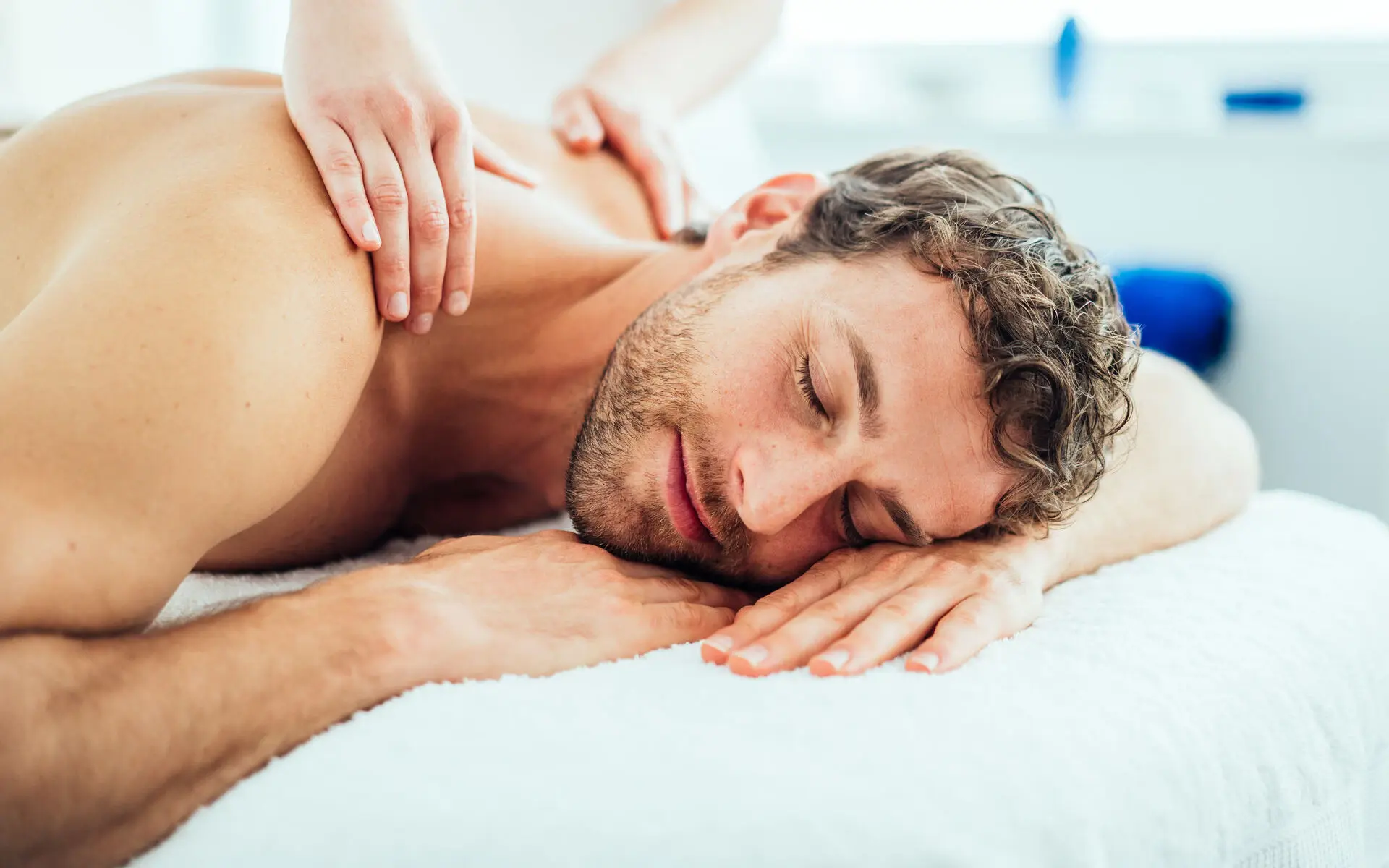 Anwendung im NIVEA Haus Grömitz Zwei Hände massieren einen Männerrücken in der Nahaufnahme. Das Gesicht des Mannes ist auf seinen Händen abgelegt und zur Kamera gewandt. Die Gesichtszüge wirken entspannt.