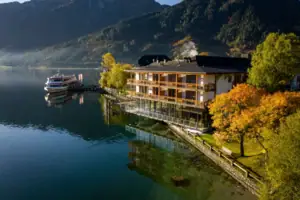aja Fürstenhaus am Achensee Gebäude am Wasser mit Bäumen und Bergen im Hintergrund.