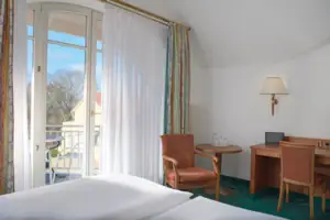 Doppelzimmer seeseitig mit Balkon Zimmer mit Bett, Schreibtisch und Stuhl.