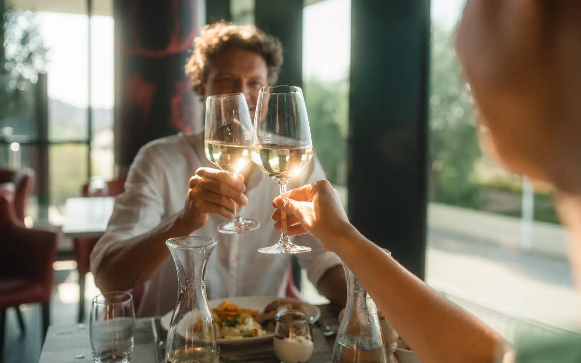 Wein Ein Paar sitzt an einem Esstisch in einemRestaurant und stößt mit Weißwein an.
