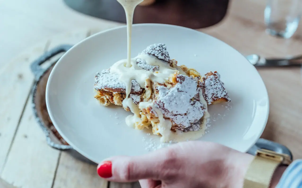Eine Frau hält einen Teller mit Kaiserschmarren in ihrer Hand und gießt Vanillesauce darauf.