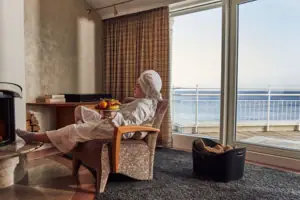 Eine Frau in einem weißen Bademantel sitzt in einem Stuhl mit einer Schale Obst auf dem Schoß.