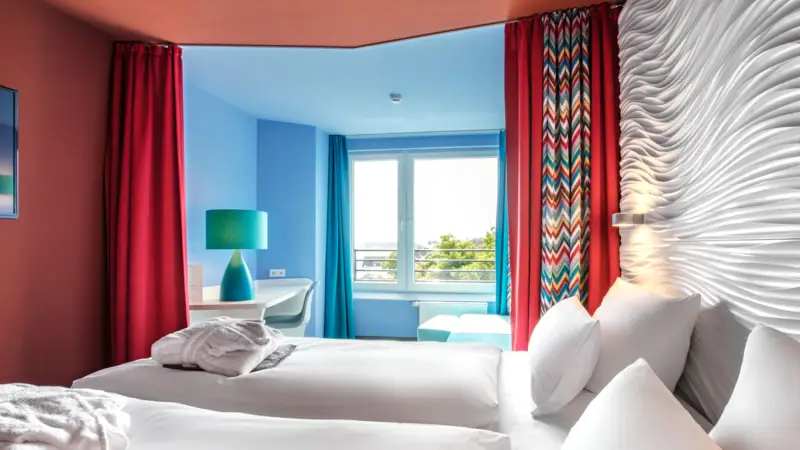 Zimmer im aja Grömitz Ein Zimmer mit zwei Betten und roten Vorhängen.