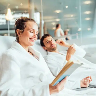 Day SPA bei aja Ein Mann und eine Frau in Bademänteln lesen ein Buch.