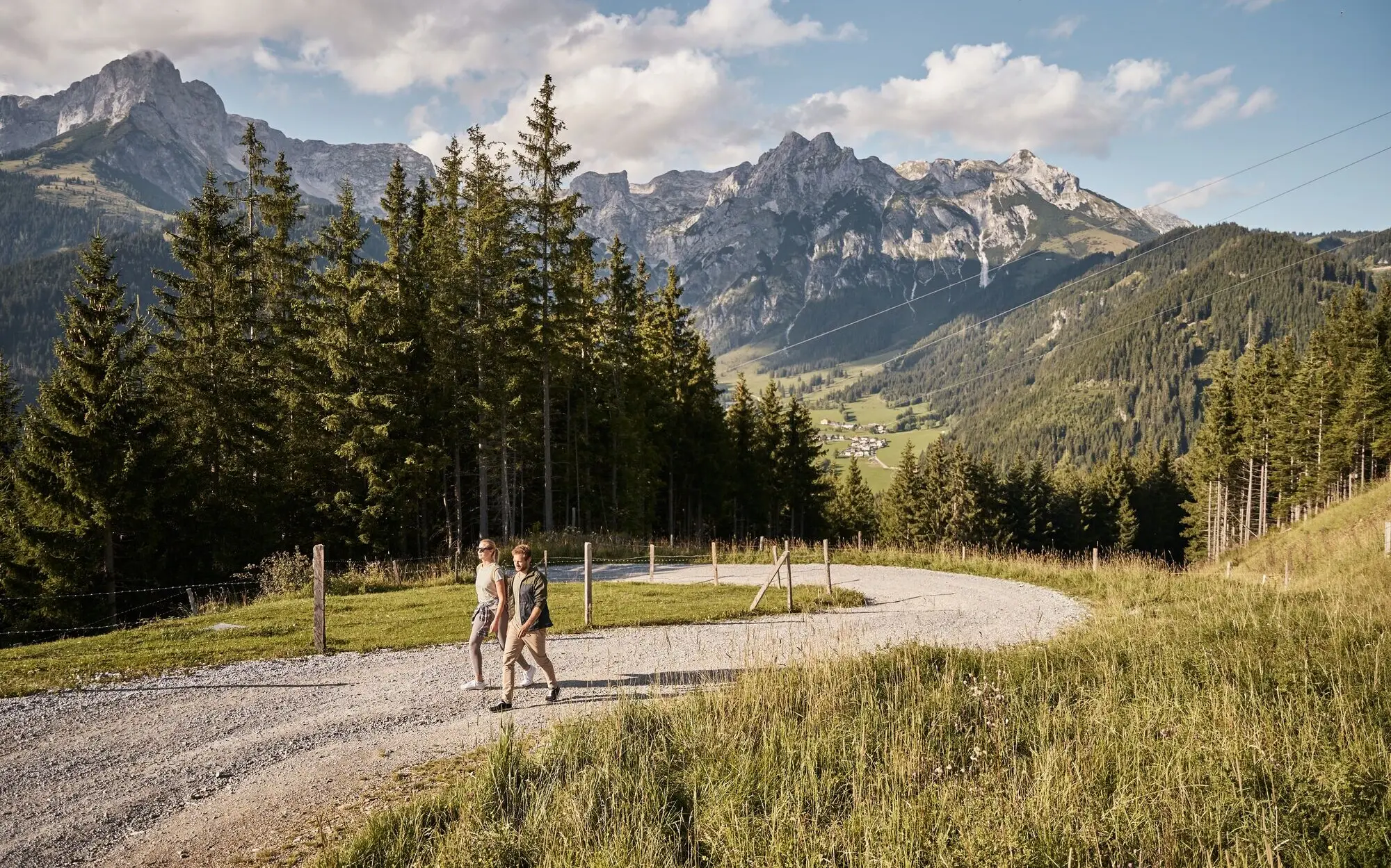 Wandern in Werfenweng Zwei Personen gehen auf einem Schotterweg vor einer Bergkette.