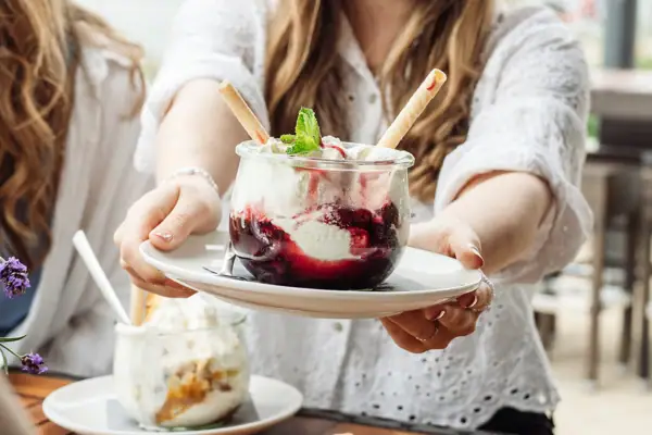 Eis im aja Warnemünde Eine Frau hält einen Teller mit einem Eisbecher mit Vanilleeis und Kirschen..