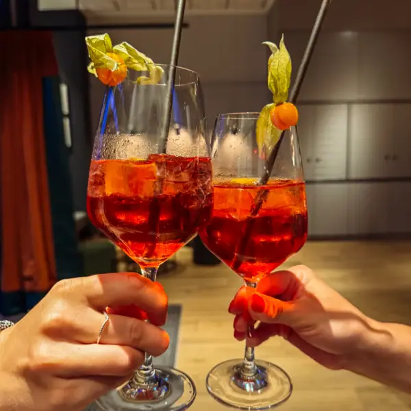 WM Fieber Hände halten Gläser mit orangefarbenem Getränk und Strohhalmen.