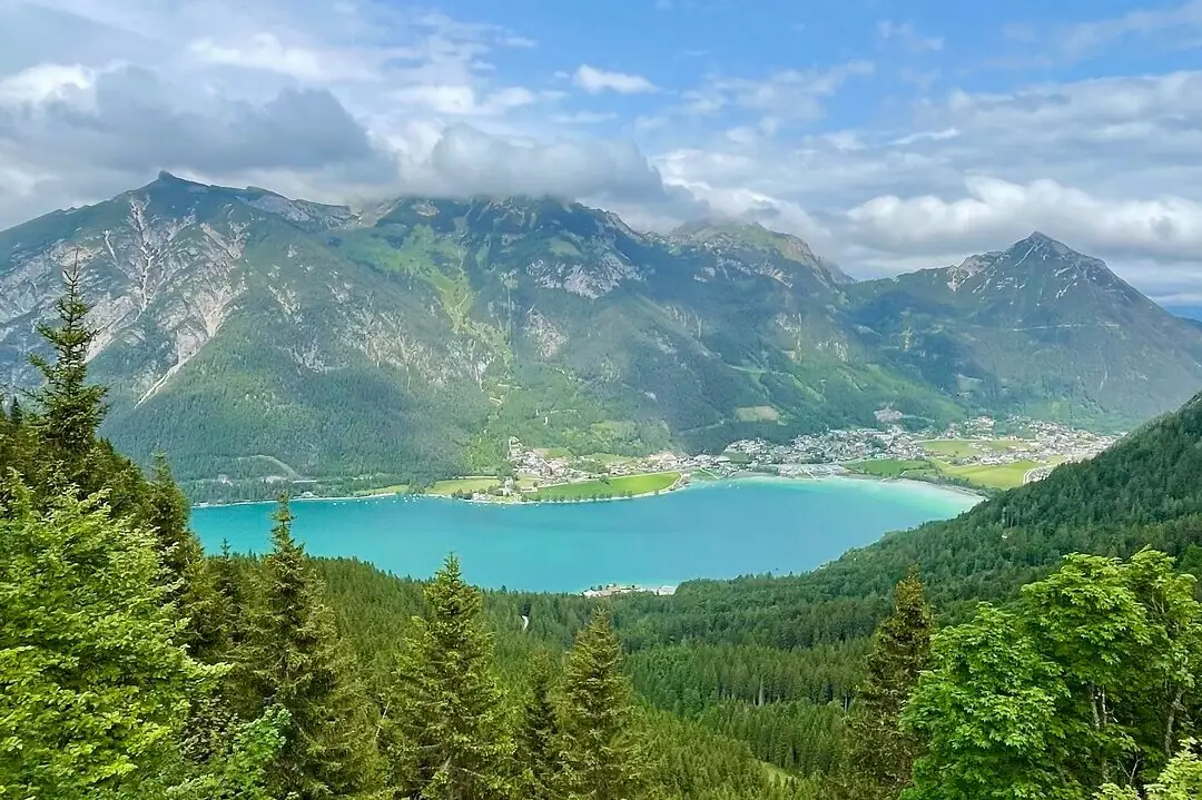 Blick auf den Achensee Ein See umgeben von Bäumen und Bergen.