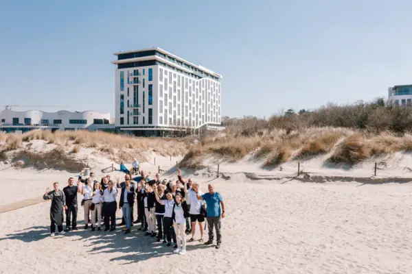 Team aus dem aja Warnemünde Eine Gruppe aus Menschen vom Team des Hotels posiert für ein Foto vor dem aja Warnemünde Gebäude.