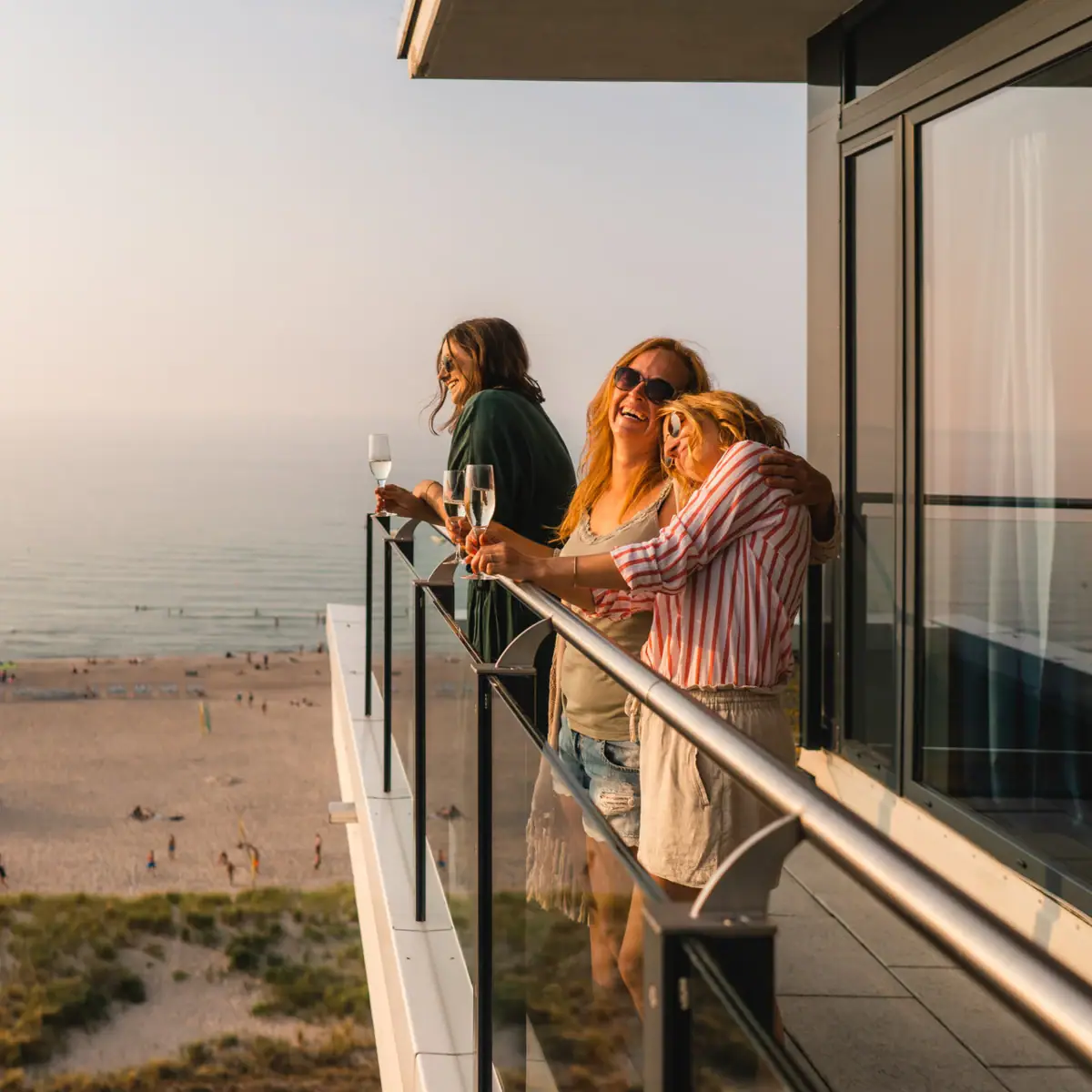 Balkon im aja Warnemünde Eine Gruppe von Frauen steht auf einem Balkon mit Blick auf den Strand.