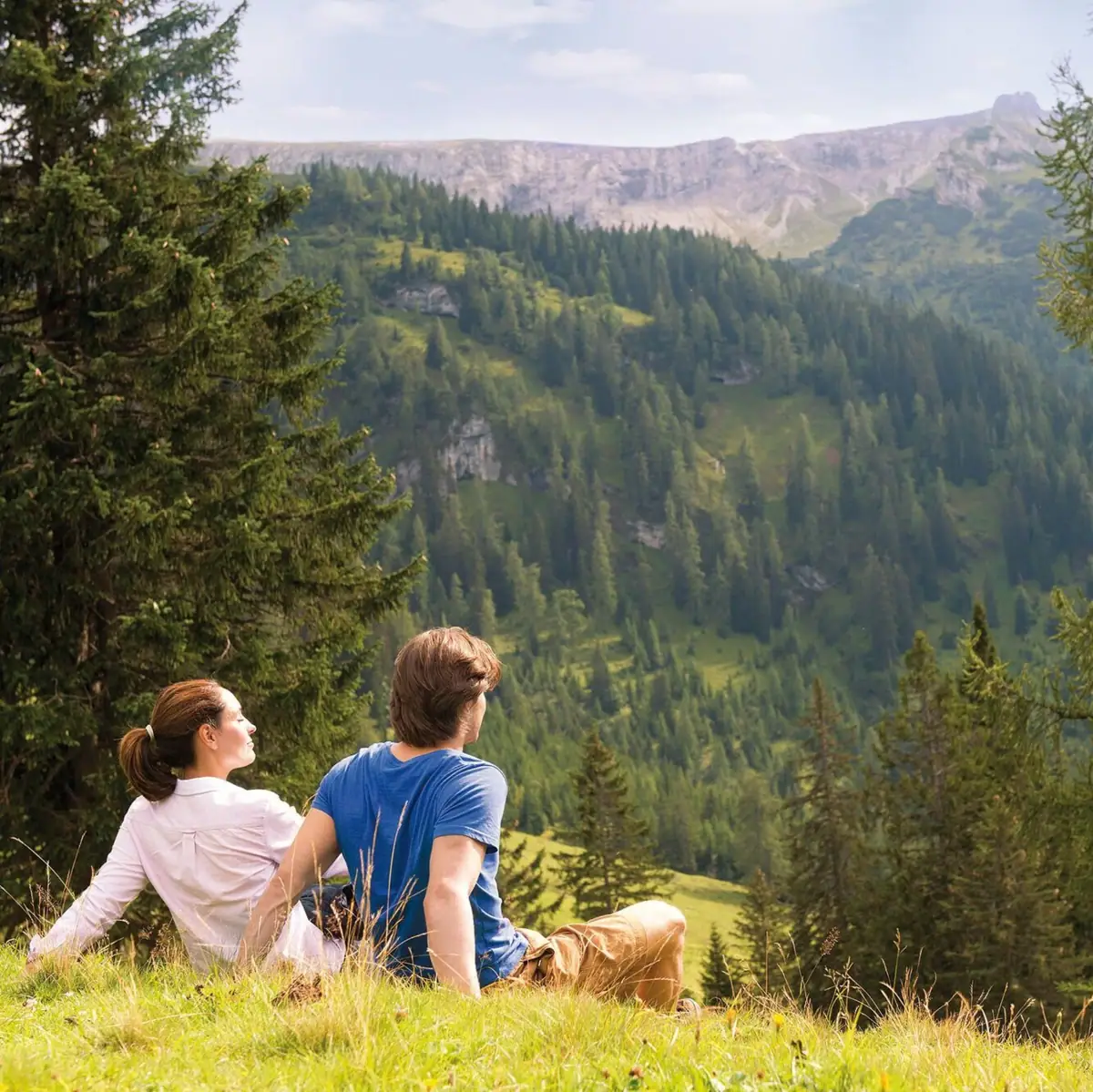 Berge Ein Mann und eine Frau sitzen auf einem Hügel und blicken auf einen Berg.